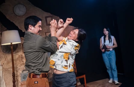 A young man and older woman fight in a domestic setting while a younger woman looks on.