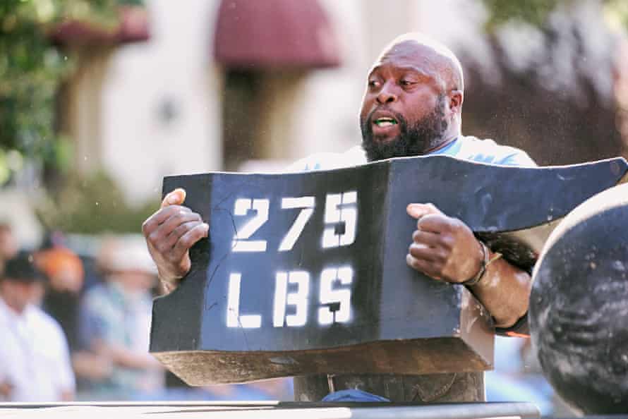 bald, bearded man holding anvil marked ‘275 lbs’