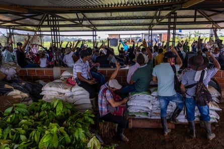 A group of people, some with raised arms., sit under a tin shelter.