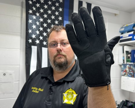 Jailer Justin Hall raises a black electric shock glove toward the camera indoors