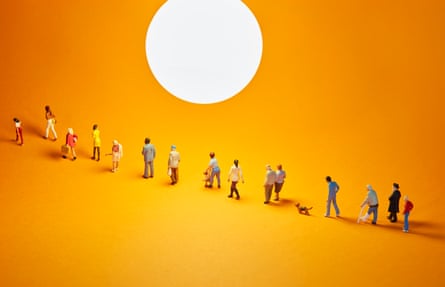 Staged photo of miniature figures walking in a line across an orange floor and backdrop with a light representing the sun