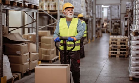 Older male worker in uniform in the warehouse with pallet truck.