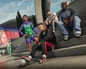 Four people dressed in casual sports gear sit on some steps, with one controlling a football under his foot.