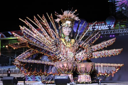 An embellished statue of a person wearing features and a headdress playing the drums