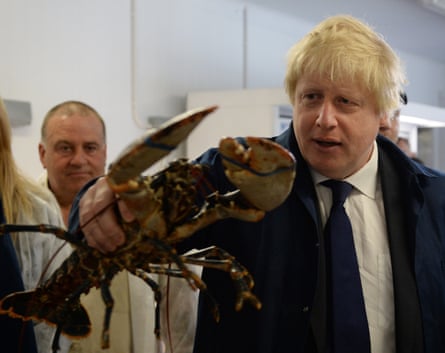 A man with shaggy blond hair and wearing a blue suit and tie holds a huge lobster.