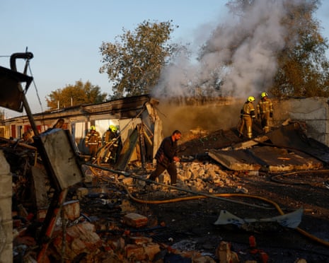 Firefighters work while residents walk past the site of private car garages hit by a Russian missile strike in Kyiv, Ukraine.