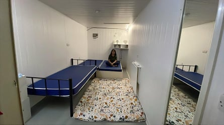 A girl sits on a bed in a small room almost filled with three beds