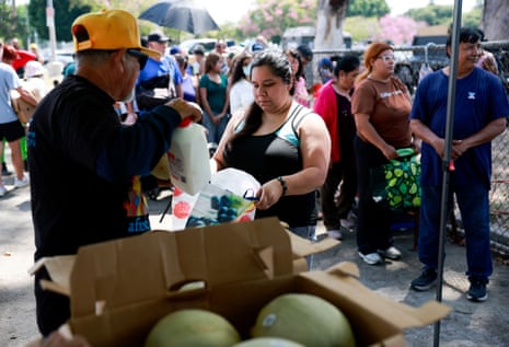 A man places a jug of milk into a bag for a woman while people stand in line behind her.