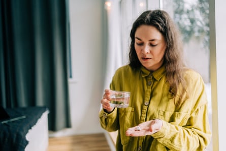 Woman holding glass of water in one hand and white tablets i another