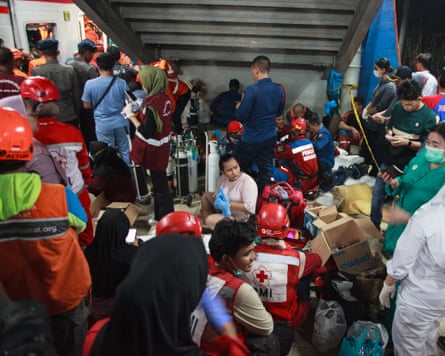 A dense scene of people as medical staff and rescue workers prepare on a rail platform next to the collision site
