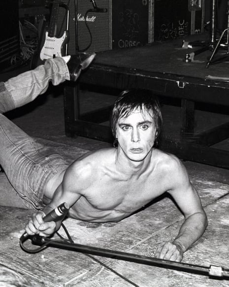 Iggy Pop lies on the stage, microphone in hand