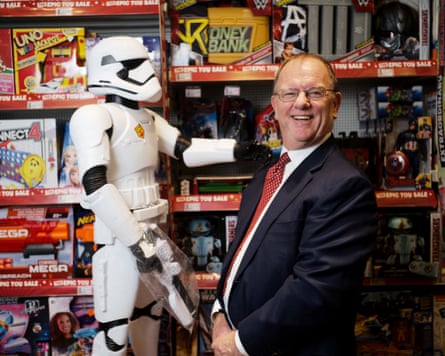A man in a blue suit laughs as he stands next to a Star Wars Stormtrooper model inside a toy shop