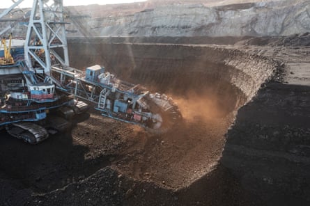 A huge, heavy machine with caterpillar tracks and a rotating wheel cuts into the coalface at the mine; light is shining on the wheel as it rotates.