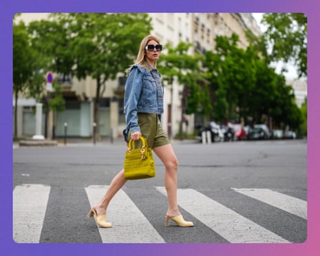 A woman in a denim jacket and olive shorts crosses a pedestrian crossing carrying a yellow handbag