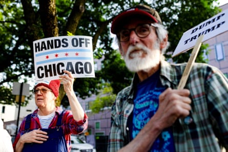 People hold signs that read ‘Hands Off Chicago’ and ‘Dump Trump’