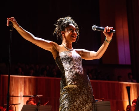 Corinne Bailey Rae performing at the Southbank Centre in London in January 2025, wearing a sparkly silver and gold dress, and with the mic in her left hand and right arm outstretched, resting on the mic stand