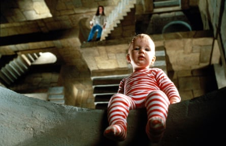 A baby in a striped onesie sits on the edge of a step looking downwards.