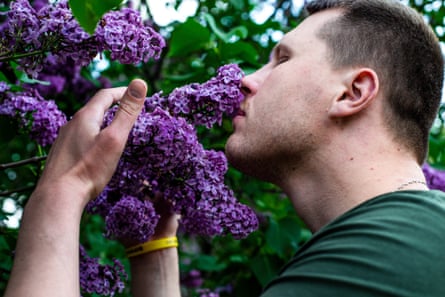 A man in a green T-shirt smells lilacs