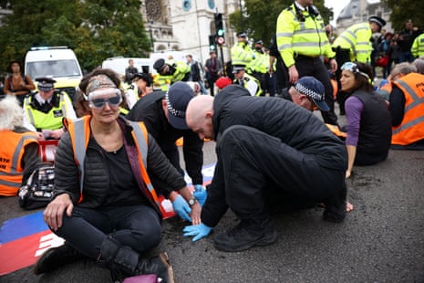 Police officers removing glue from the hand of a protester as Insulate Britain activists blocked the road outside the Houses of Parliament today.