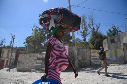 A pregnant woman with a large bag balanced on her head walks down the street