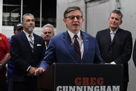 Mike Johnson speaks at a podium during a campaign stop, flanked by several men in suits
