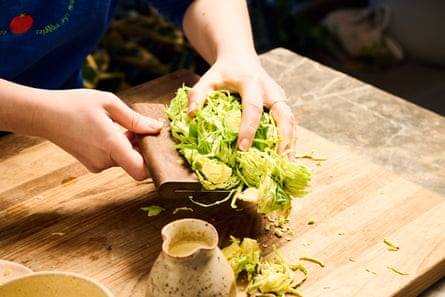 The cook gathers shredded brussels sprouts from a chopping board in preparation to add to the dish she is preparing