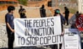 Two people hold a white sign reading 'The people's injunction to stop Cop City' as police officers stand behind them.