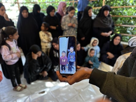 Palestinians mourn for the two children with one holding a phone with pictures of them
