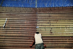A migrant looks at US border patrol officers through holes in the border wall between the US and Mexico.