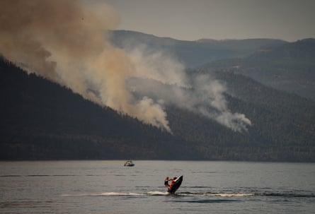 A person rides a personal watercraft on Okanagan Lake, in Lake Country, British Columbia, as the Quilpituk Creek wildfire burns on the mountainside behind him