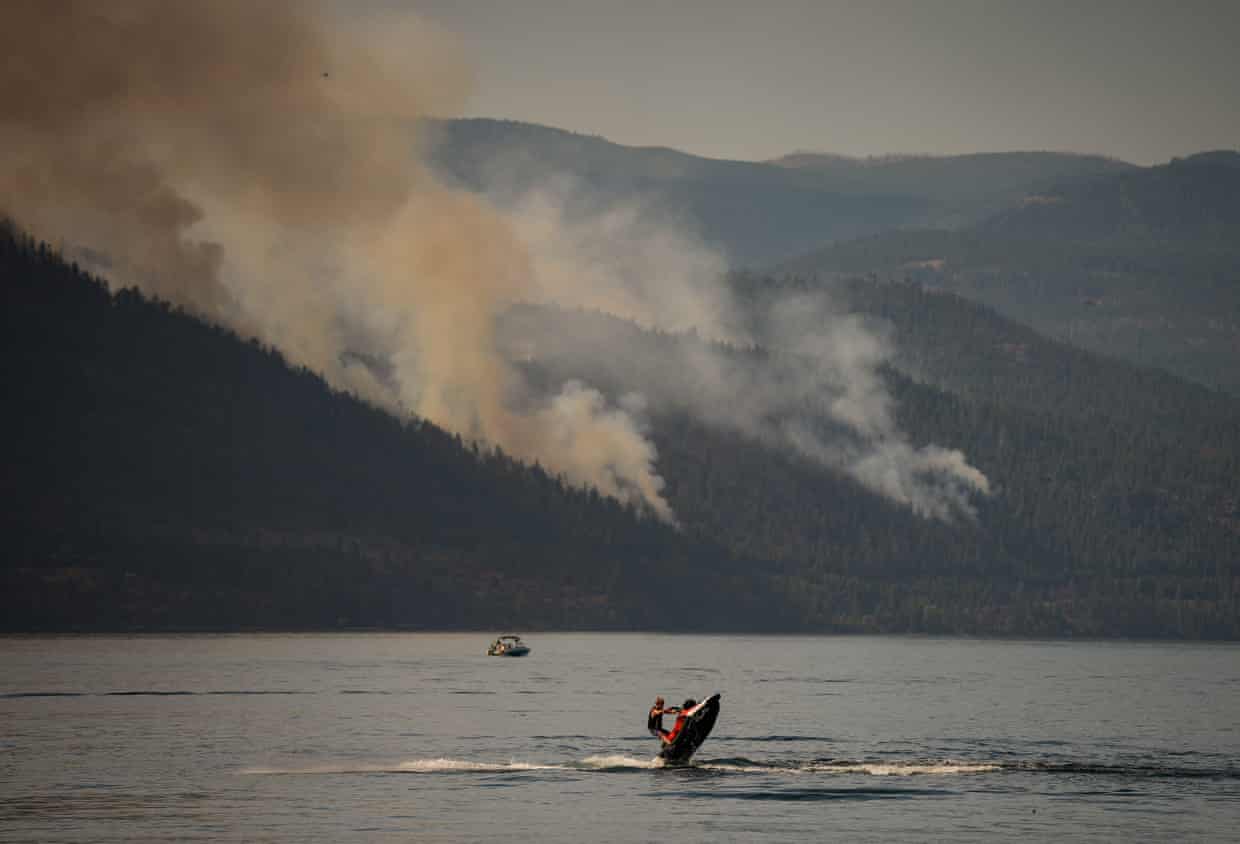 A person rides a personal watercraft on Okanagan Lake, in Lake Country, British Columbia, as the Quilpituk Creek wildfire burns on the mountainside behind him