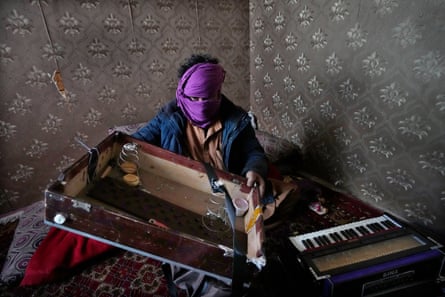 Afghan musician with his face covered by a scarf holding pieces of a broken harmonium.