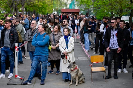 People standing in several long lines, with the woman at the head of a queue with a dog