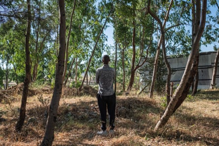A man stand with his back to the camera among some trees
