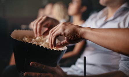Hands taking popcorn from a container at the movies.