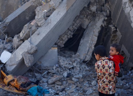 A Palestinian boy carrying a baby stands at a site of Israeli strikes in Rafah in the southern Gaza Strip.