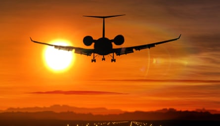 Airplane silhouette landing at an airport during sunset.