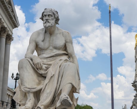 A marble statue of historian Thucydides seated and draped in robes against a cloudy blue sky