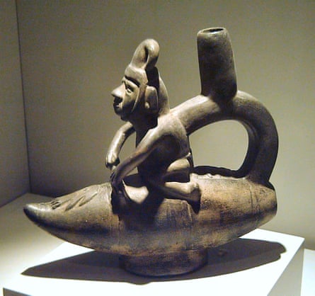 A brown ceramic jug in the shape of a person straddling a torpedo-like boat with a handle and spout running from the boat to the figure’s back.