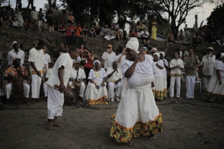 A woman of African descent dressed in white, including a white turban, dances with a man in white in the center of a circle of people.