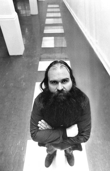A black and white image of a man with his arms crossed standing on blocks of white and looking directly at the camera