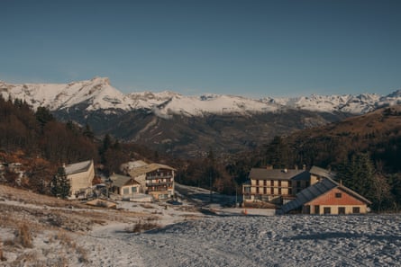 Chalets sit closed at the bottom of a slope with a thin covering of snow and scrubby grass.
