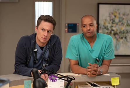 Zach Braff and Donald Faison lean on a desk in a hospital