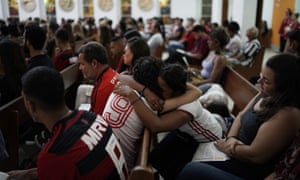 Two young women, with Flamengo football kits, embrace a mass to commemorate the victims of the fire.
