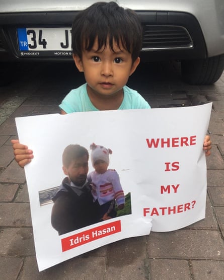 A child holds a poster carrying an image of a man holding a child with the words ‘Idris Hasan’ and ‘Where is my father?’