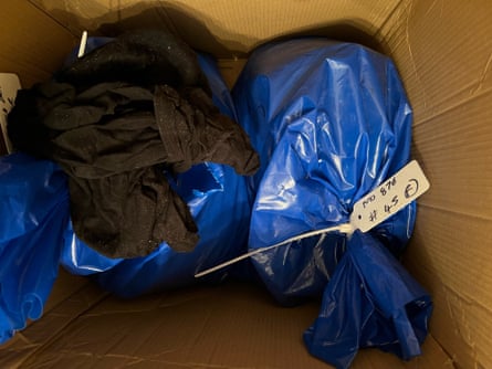 An opened cardboard box with blue plastic bags and clothing inside, viewed from above