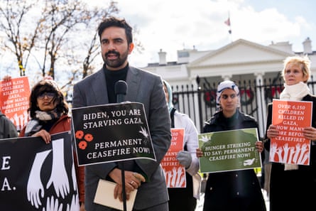a man speaks into a microphone with a sign taped to it that reads ‘Biden you are starving Gaza permanent ceasefire now’