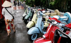 A woman walks past a row of repaired old Vespa scooters displayed for sale along a street in Ho Chi Minh