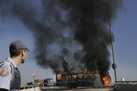 شرطي ينظر إلى حافلة بلدية أضرمت فيها النيران في ساو باولو، البرازيل، في 22 يوليو 2006، وسط سلسلة من الهجمات المرتبطة بحزب المؤتمر الشعبي العام.