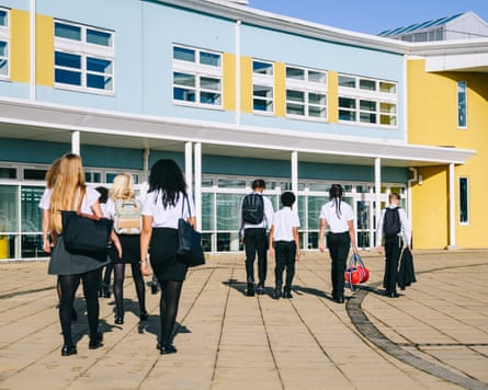 High school students wearing uniform walking to school entrance carrying bags.